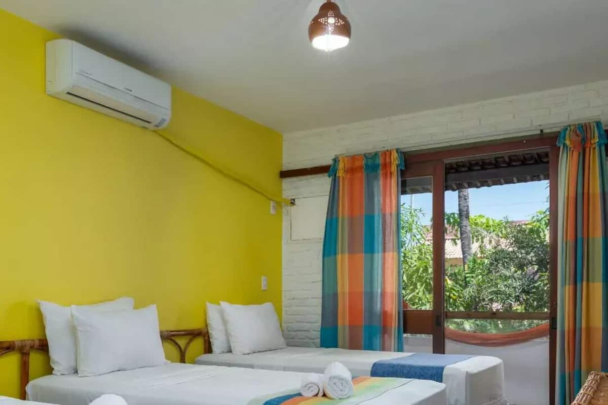 Ein Hotelzimmer mit zwei Betten, einem Fenster mit Vorhängen und einer Klimaanlage.
