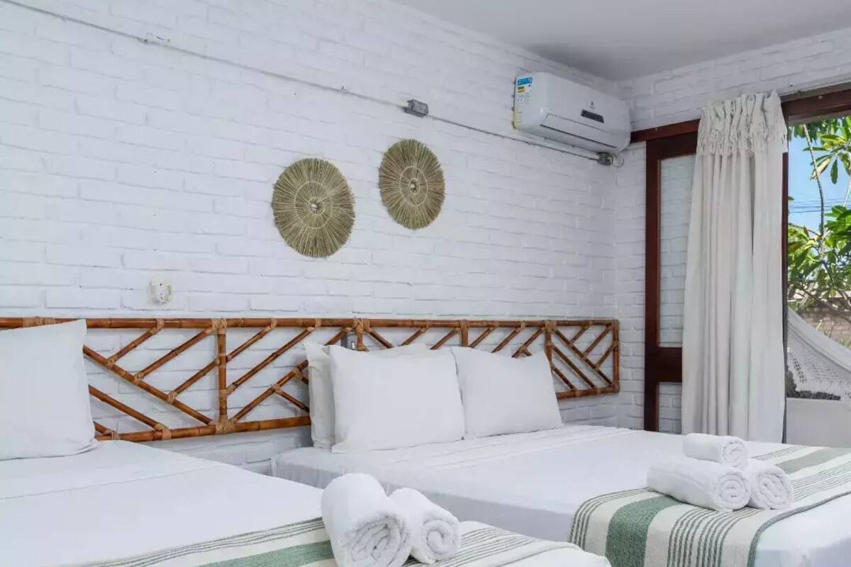 Ein Hotelzimmer mit zwei Betten, weißer Bettwäsche, einem Bambus-Kopfteil und zwei Wandbildern.