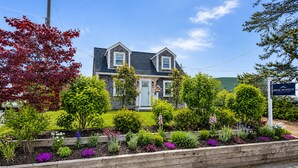 Una casa de dues plantes amb un porxo davanter, envoltada d'un jardí ben cuidat i ple de plantes i flors.