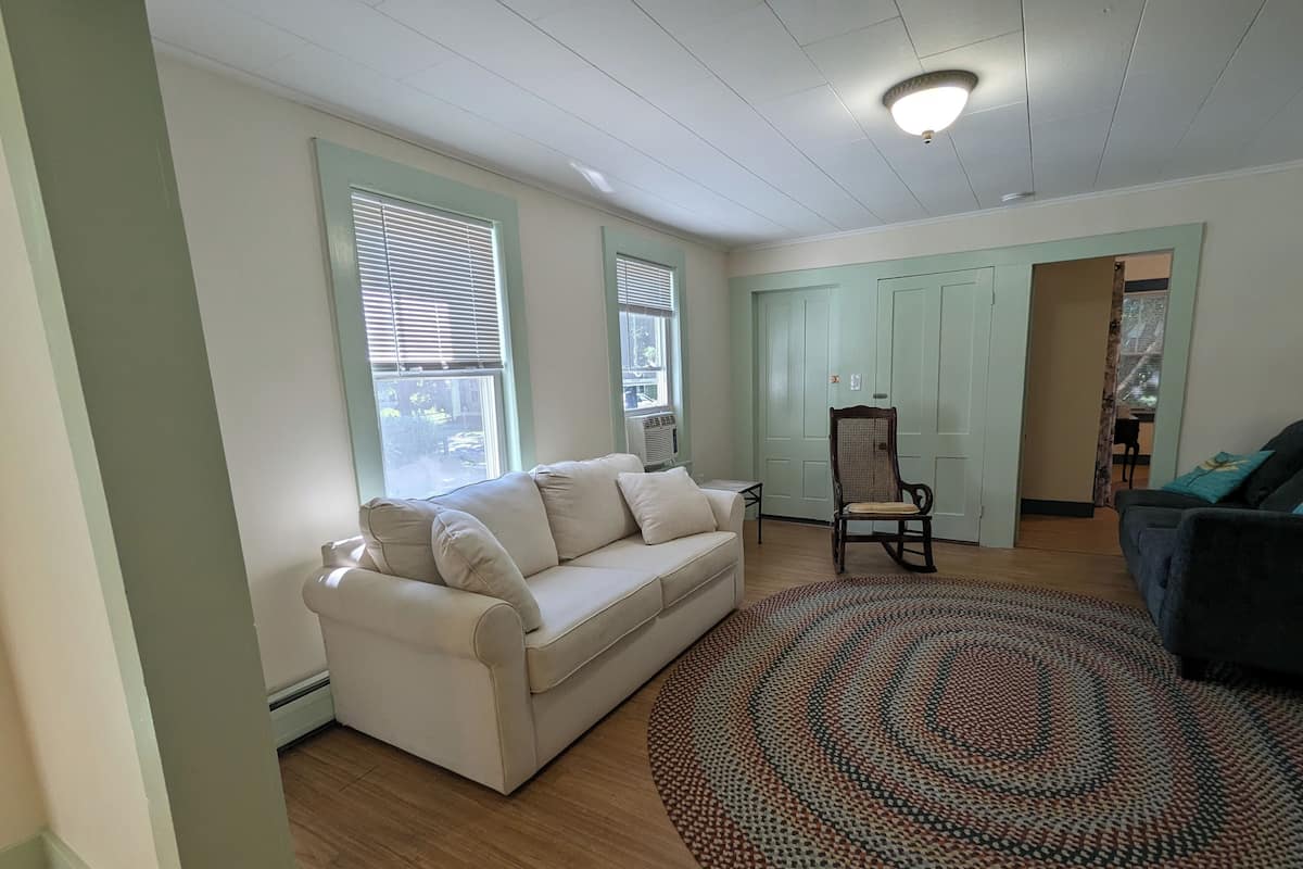 A living room with a beige sofa, a patterned rug, and a wooden floor.