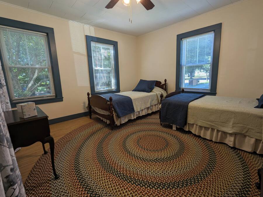 Un dormitorio con dos camas, un tapete estampado y ventanas amplias con persianas.
