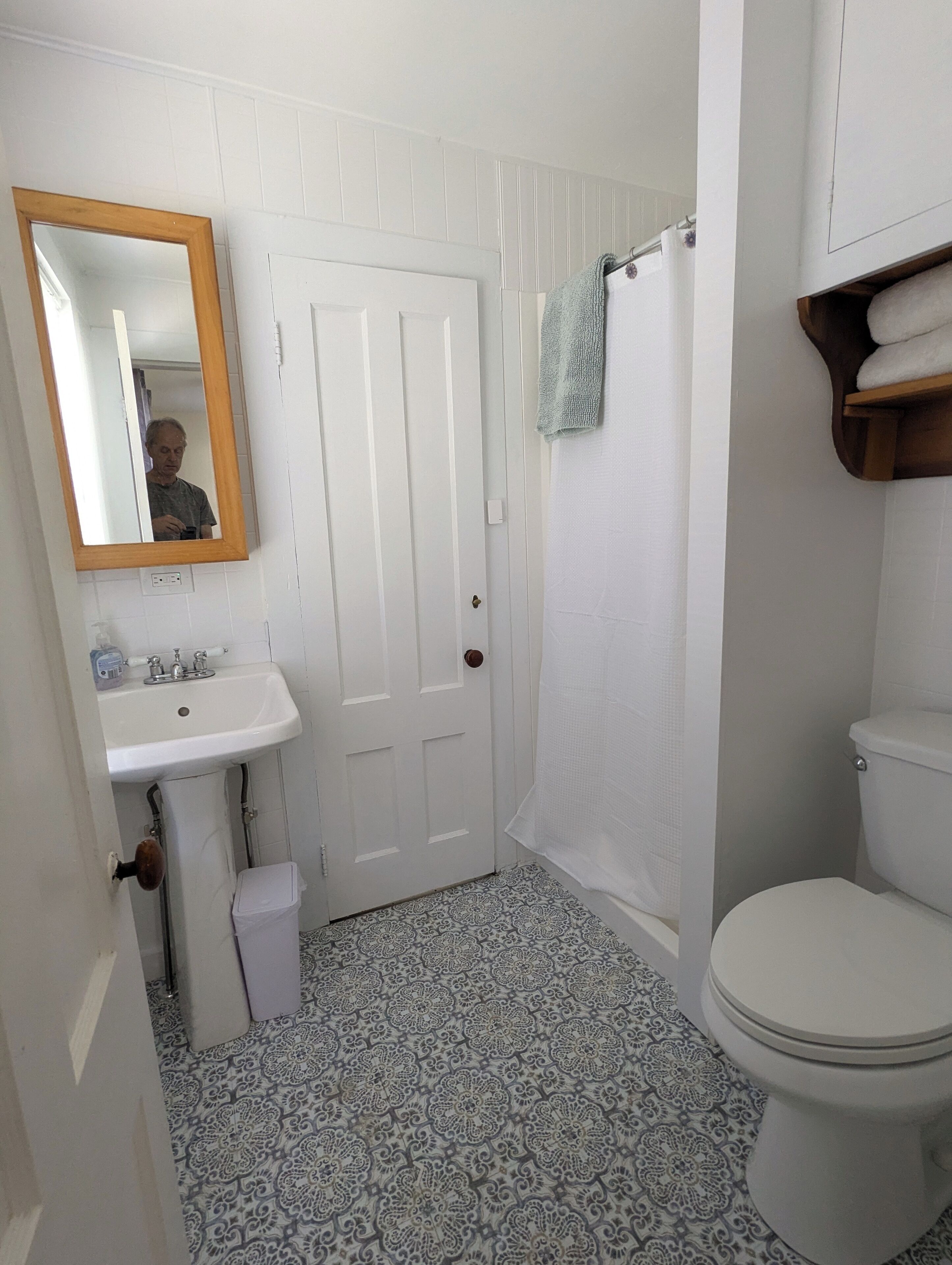 A bathroom with a white sink, a mirror, a toilet, and patterned floor tiles.