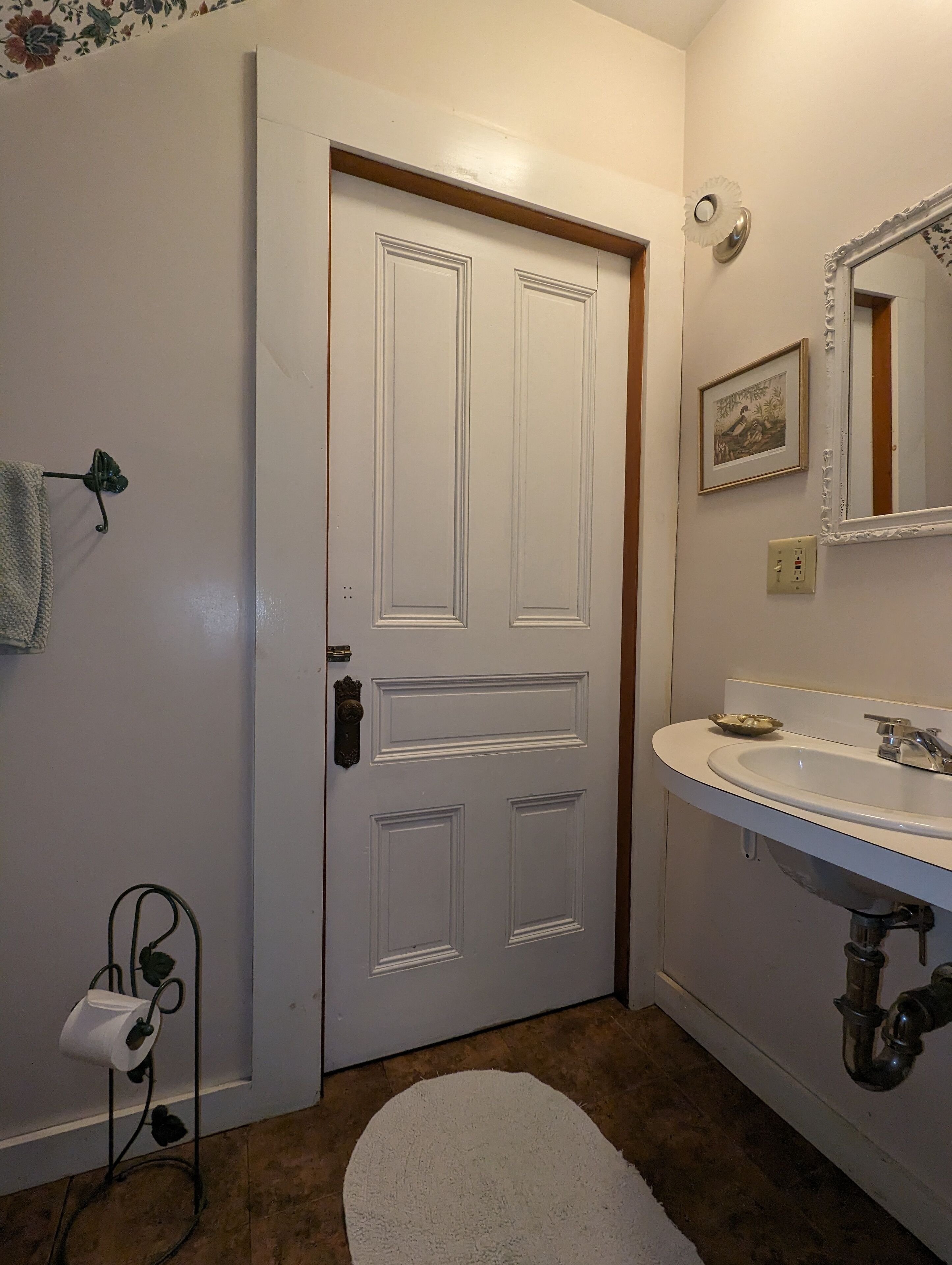 A bathroom with a white door, a sink with a mirror, and a towel rack.