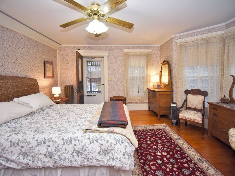 A bedroom with a large bed, a wooden dresser, a chair, a mirror, and a ceiling fan.