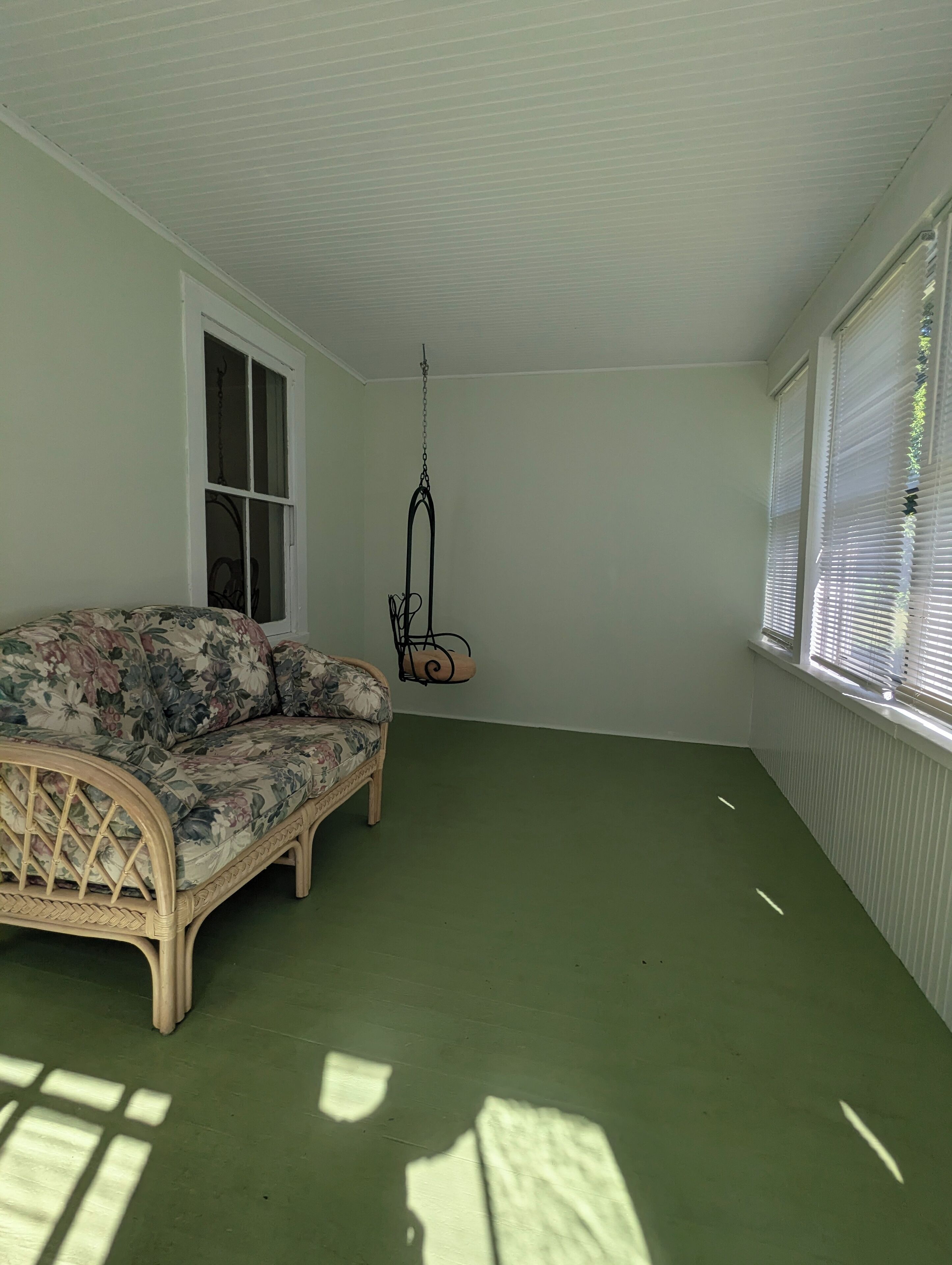 Una habitación con un sofá floral, una silla colgante, una ventana con persianas y un radiador.