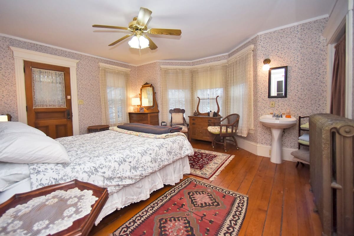 A bedroom with a bed, dresser, vanity, and a ceiling fan.