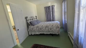 Un dormitorio con cama, ventilador de techo, ventana con cortinas y puerta que da a otra habitación.