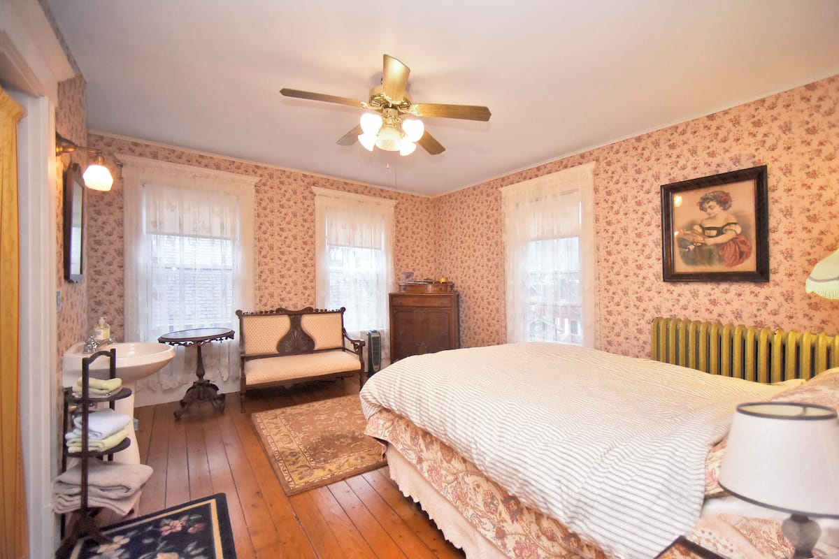 A bedroom with a bed, a chair, a dresser, a radiator, and a window with curtains.