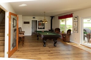 A pool room with a pool table, chairs, and a staircase leading to another room.