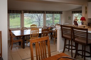 Enjoy meals in this dining area with a large table and comfortable seating, offering a view of the lawn and trees.