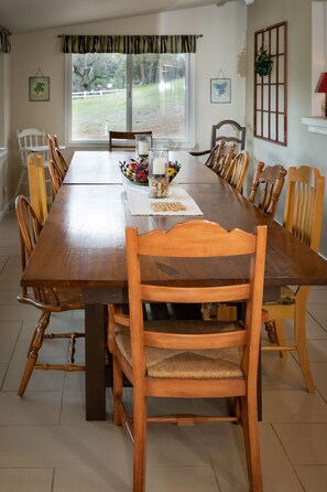 A dining room with a long wooden table, multiple chairs, and a window with a view of the outdoors.