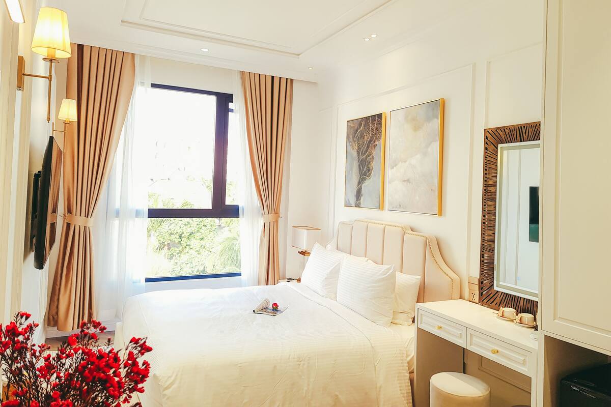 A hotel room with a large bed, a bedside table, a mirror, and a window with curtains.