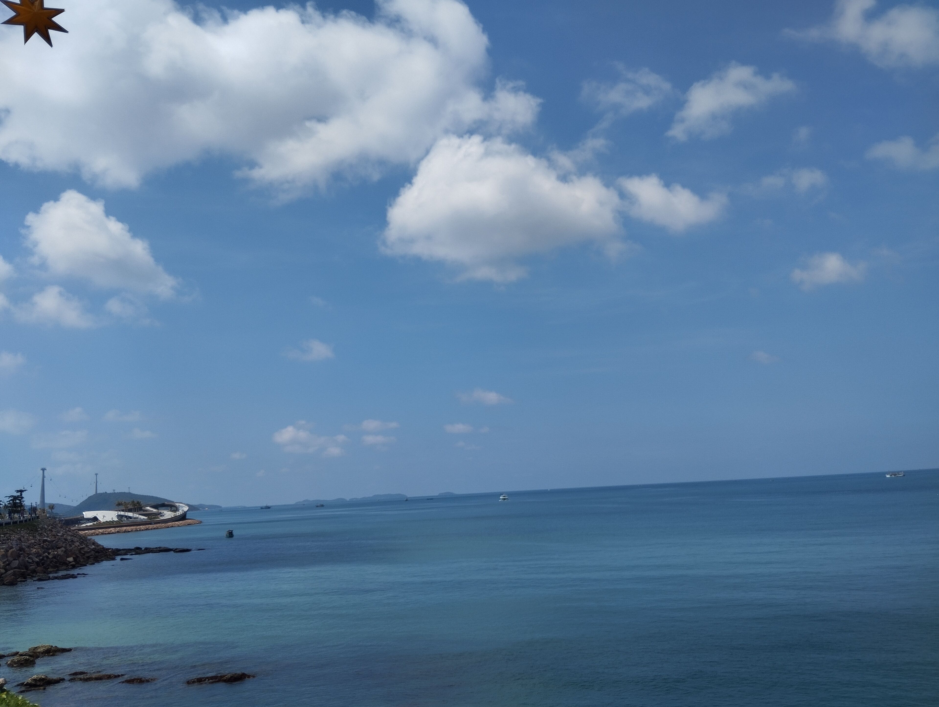 Eine Küstenansicht bei blauem Himmel, ruhiger See und einer kleinen Insel mit Gebäuden.