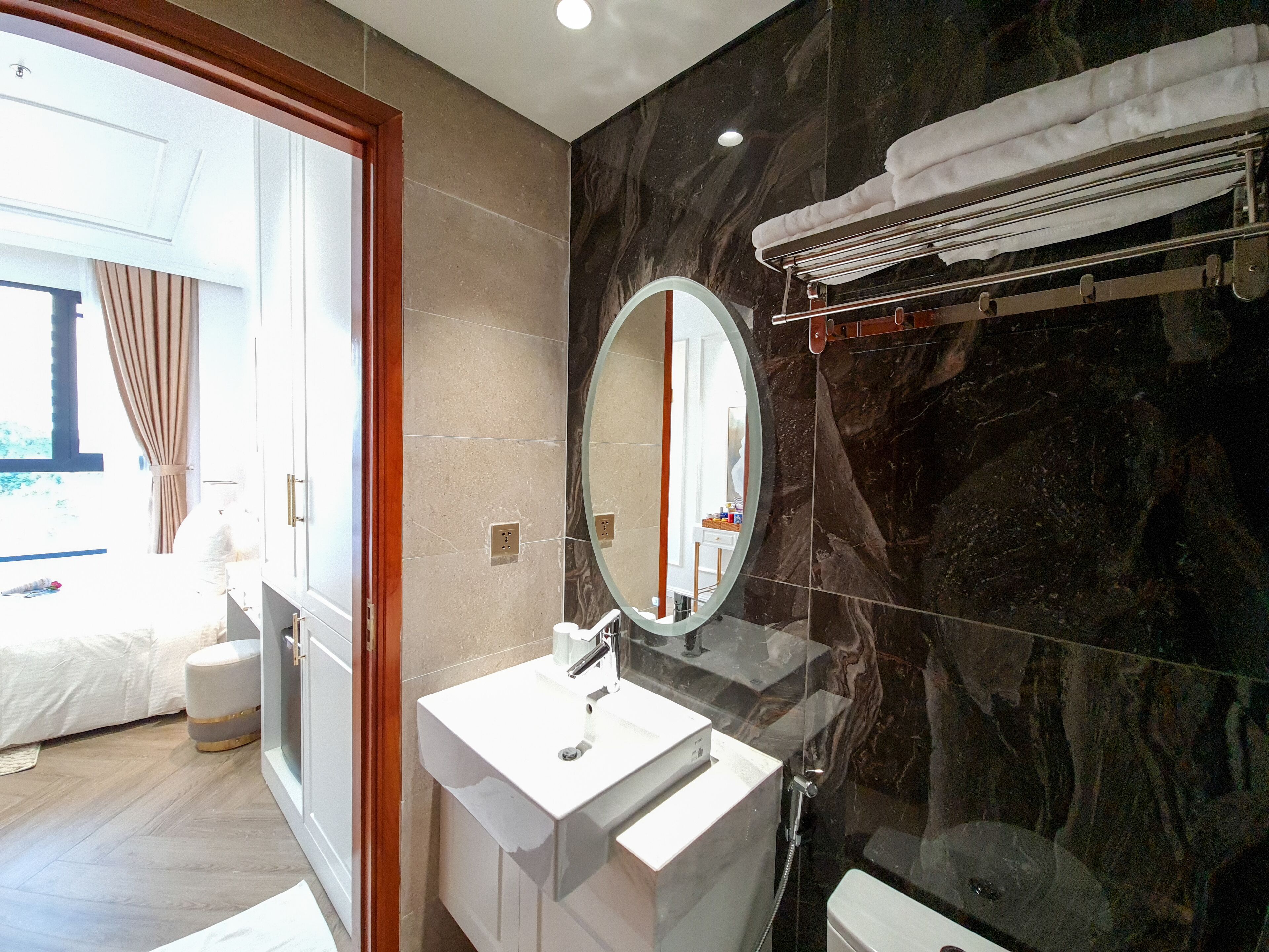 A modern bathroom with a marble wall, a round mirror, a white sink, and a towel rack.