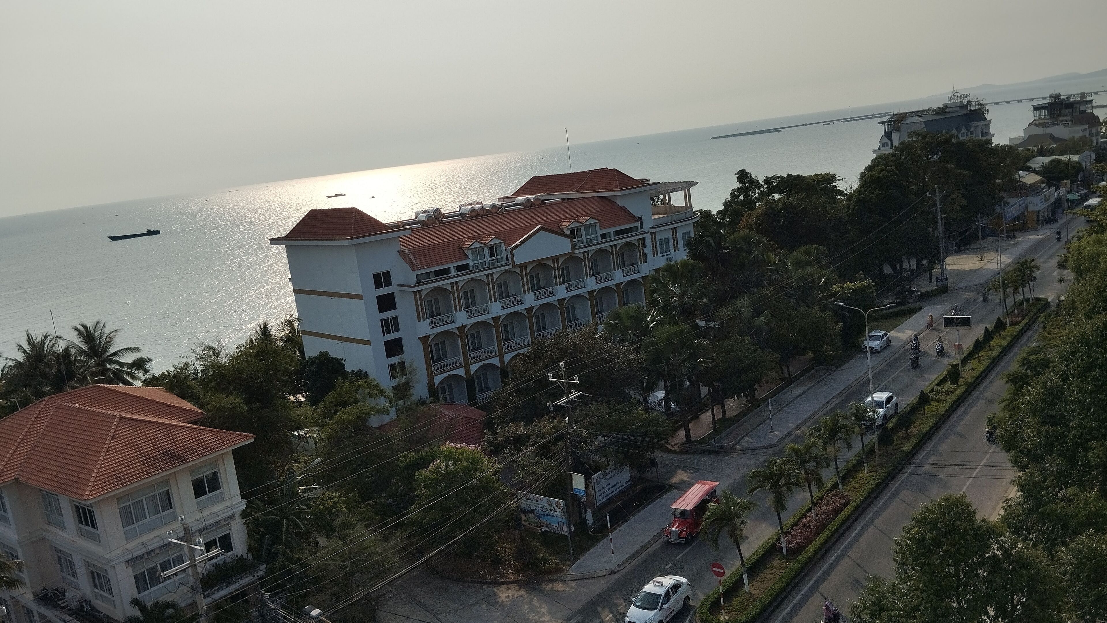 A multi-story building with a red-tiled roof, located near a waterfront with a view of the sea.