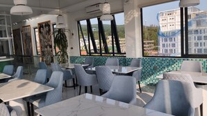 A restaurant with marble-topped tables and chairs, large windows with a view of buildings and hills, and a tiled backsplash. - PHUC THANG HOTEL (Phu Quoc)