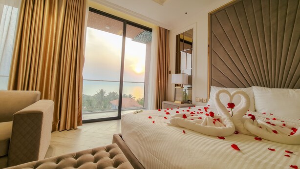 A hotel room with a bed, a chair, a nightstand, and a view of the sunset. - PHUC THANG HOTEL (Phu Quoc)