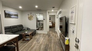 Un espace de vie compact comprenant un canapé, une table basse et un coin repas. On aperçoit une cuisine avec un miroir et un téléviseur à l’arrière-plan.