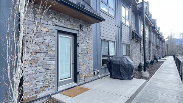 Une maison de ville moderne avec une façade en pierre, de grandes fenêtres et un espace barbecue couvert.