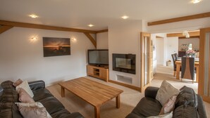 Een moderne woonkamer met een bank, een salontafel, een televisie en een eethoek met stoelen en een tafel.