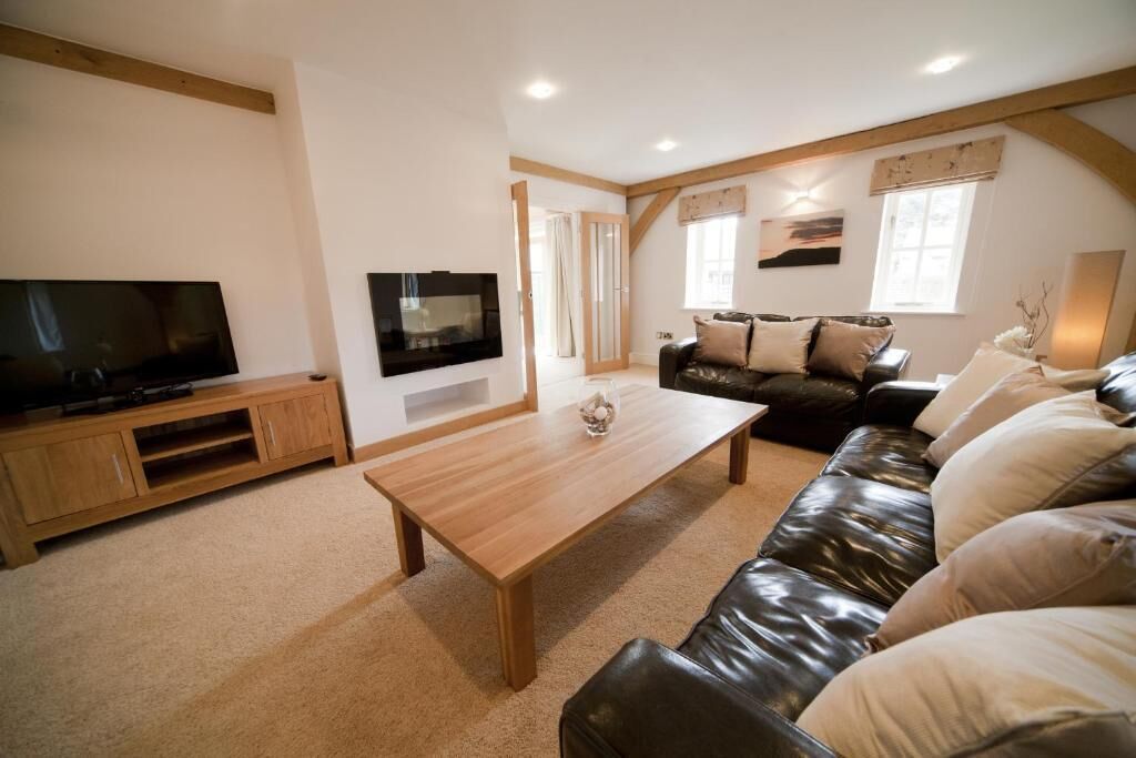 A living room with a wooden coffee table, a leather sofa, a TV on a wooden stand, and a window with curtains.