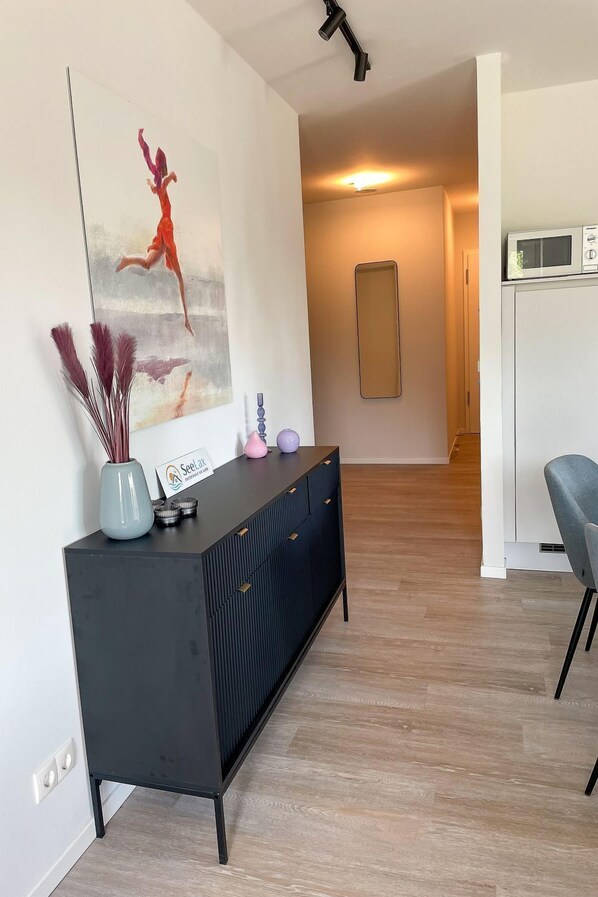 A modern living room with a black console table, a large abstract painting, a vase with pampas grass, a pink vase, and a sign. - 2913 - Seelax - 2913 - Seelax - Strandwiese 1 - Apartment 3 (Dahme)