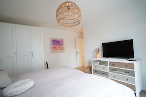 Une chambre à coucher avec un lit, un téléviseur posé sur une commode et un luminaire suspendu au plafond, fait en osier.