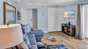 A living room with a sofa, a coffee table, a TV, and a lamp. - Sunrise & Sunset Oceanfront Condo (Ocean CIty)