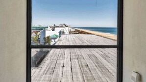 A room with a large window overlooking a wooden deck and beach. - Sunrise & Sunset Oceanfront Condo (Ocean CIty)