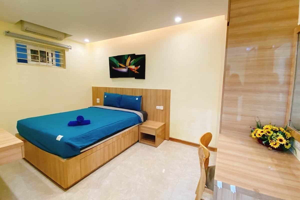 A modern bedroom with a wooden bed, a nightstand, a small table, and a wall-mounted artwork.