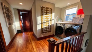 A laundry area with two washing machines, a wooden floor, a window with a view, and a door leading to another room. - 1912 Historic Ballard Craftsman
5 Bed • 2 Bath • Yard • Parking (Seattle)