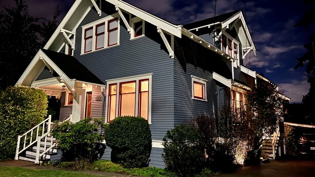 A two-story house with a steep gable roof, a front porch with a staircase, and a well-maintained lawn. - 1912 Historic Ballard Craftsman
5 Bed • 2 Bath • Yard • Parking (Seattle)