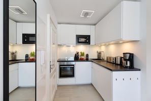 A modern kitchen with white cabinets, a built-in oven, a microwave, and a coffee maker. - Strandwärts - Modern app. with balcony, sea view, parking space, WLAN. (List)