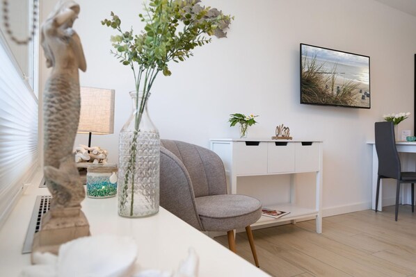 A modern living room with a white sofa, a glass vase with flowers, a statue, and a painting on the wall.
