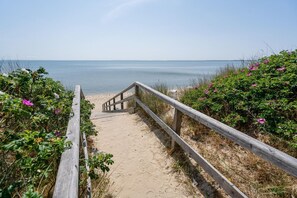 A wooden staircase leading to a sandy beach with a view of the sea.