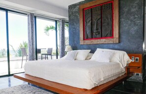 A modern bedroom with a large bed, a view of palm trees, and a statue on the wall.