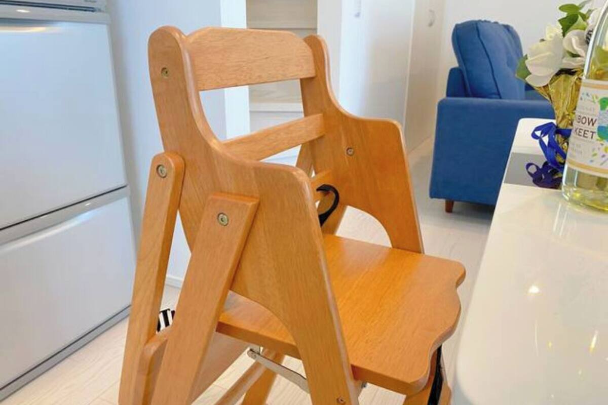 Puinen tuoli, jossa on korkea selkänoja ja käsinojat, on sijoitettu moderniin keittiöön. Keittiössä on valkoiset kaapit ja taustalla näkyy sininen tuoli.
