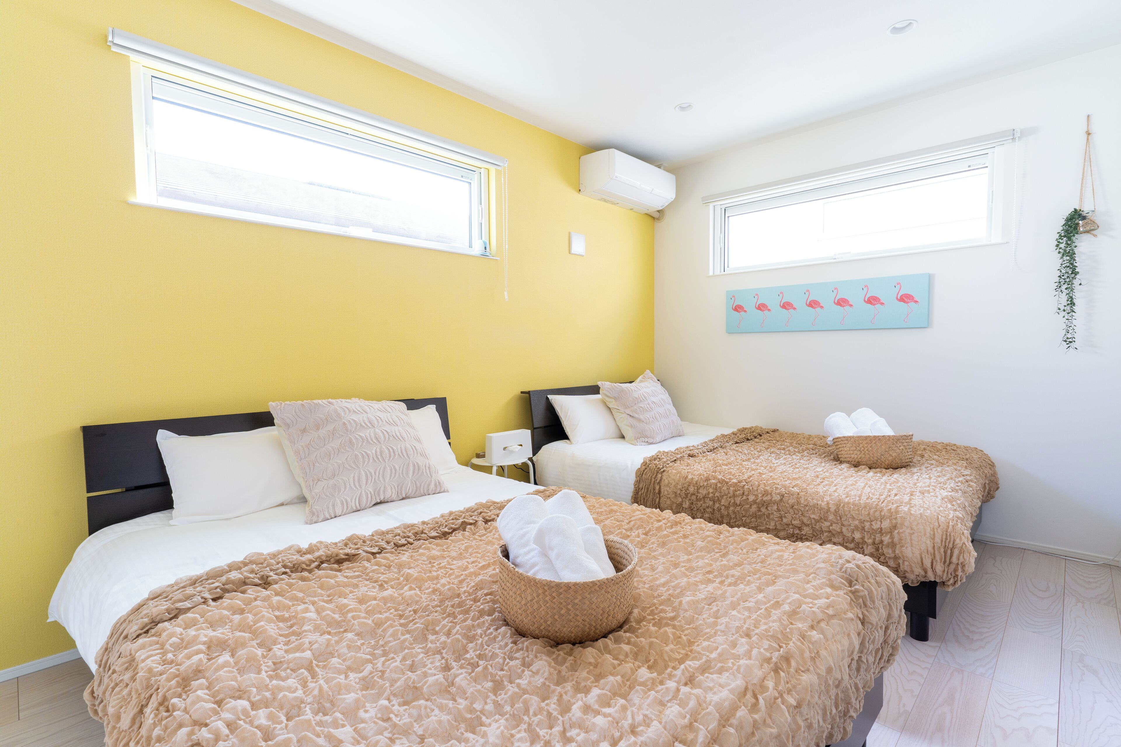 A hotel room with two beds, a yellow wall, and a painting of flamingos.