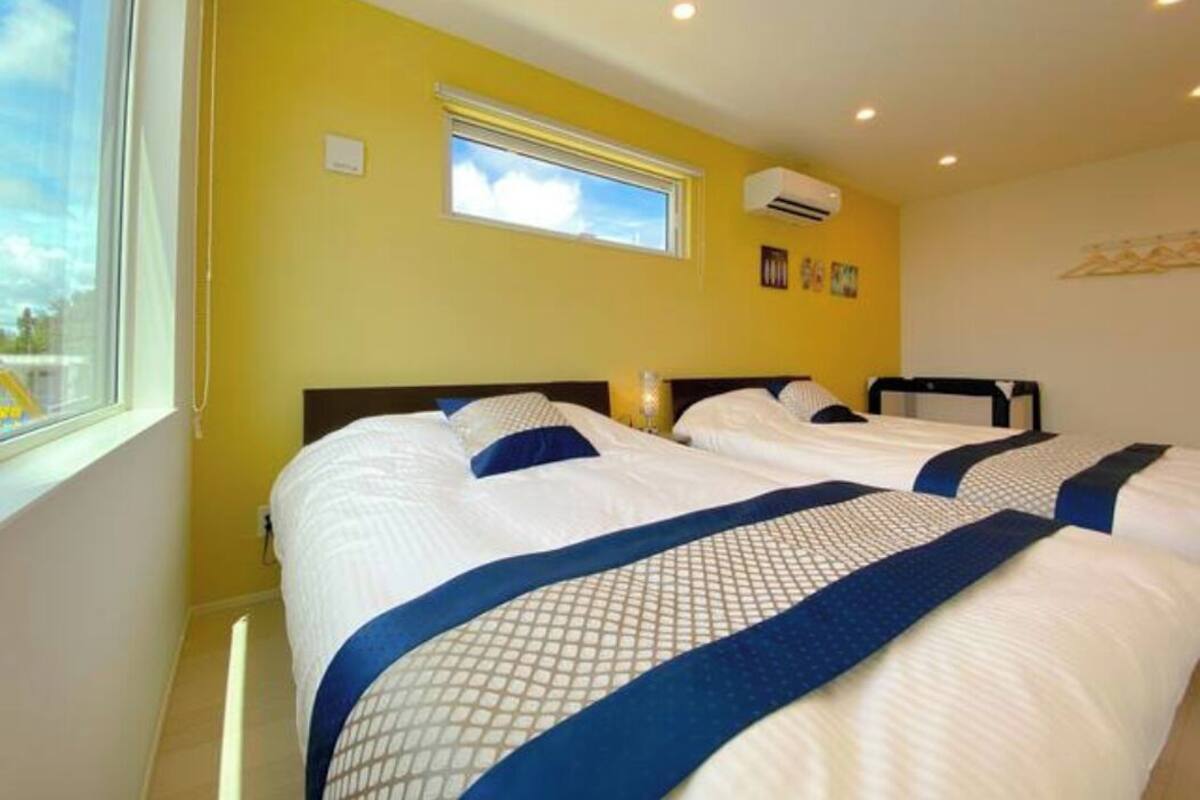 Hotellihuone, jossa on kaksi sänkyä, ikkuna ja ilmastointilaite.
