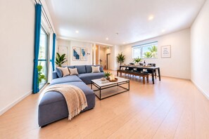 A modern living room with a sectional sofa, a coffee table, and a dining area with a table and chairs.