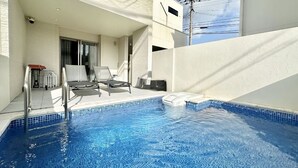 A swimming pool with lounge chairs and a table, surrounded by a white building with a glass door. - Grandioso Okinawa Pool Villa Onna 7 (Onna)