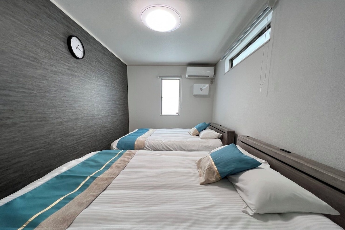 A hotel room with two beds, a clock on the wall, and an air conditioning unit.