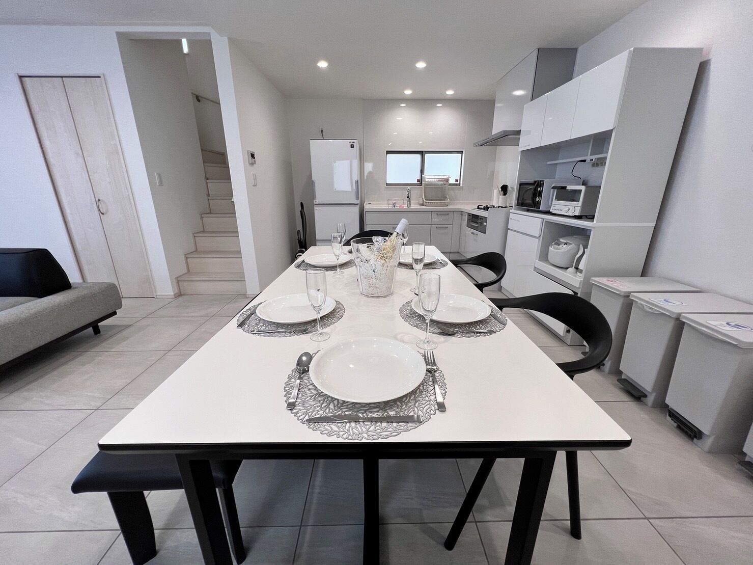 A modern kitchen with white cabinets, a dining table set for four, and a staircase leading to an upper level.