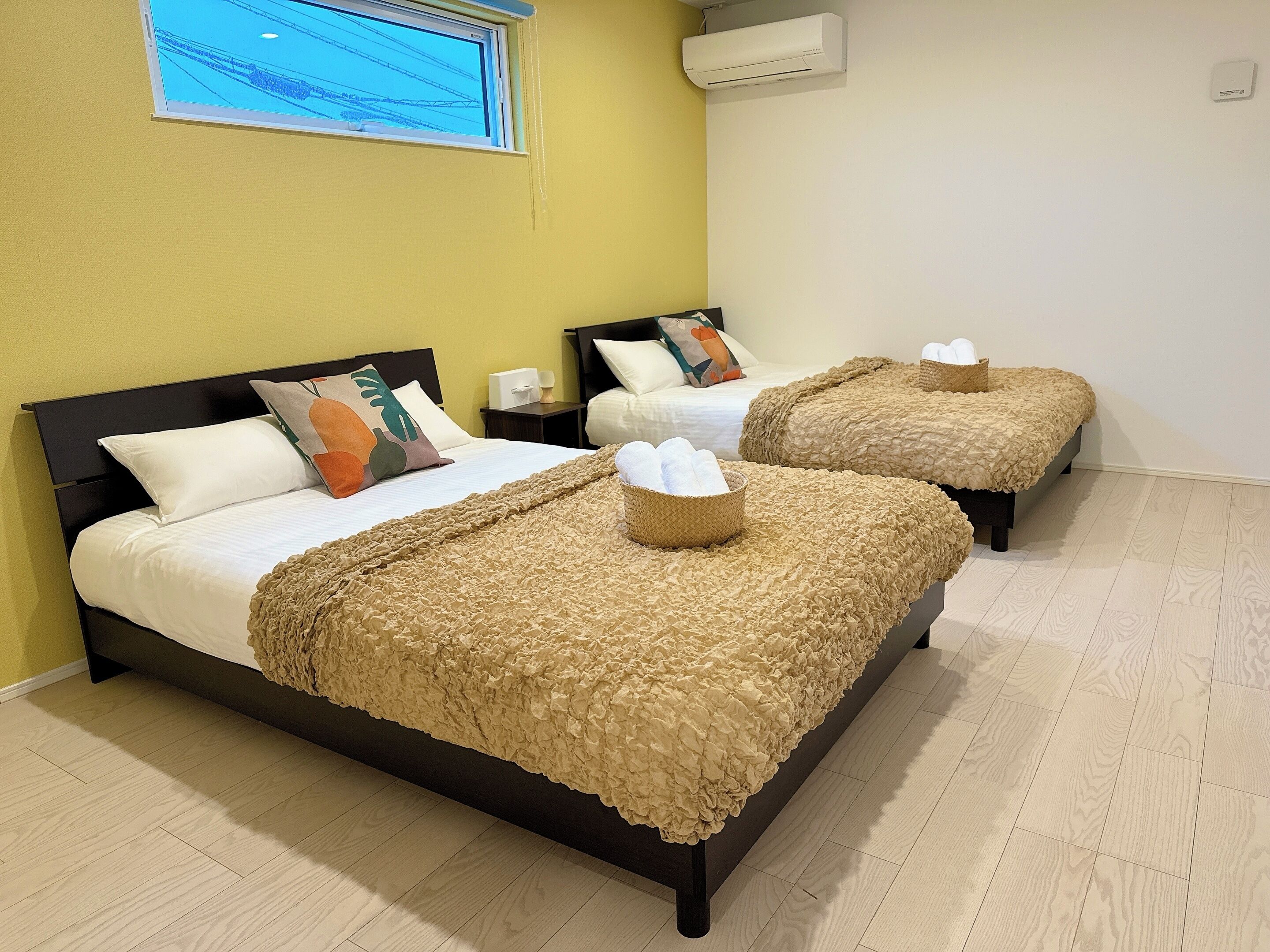 A hotel room with two beds, each with a ruffled beige blanket and a pillow with a leaf design.