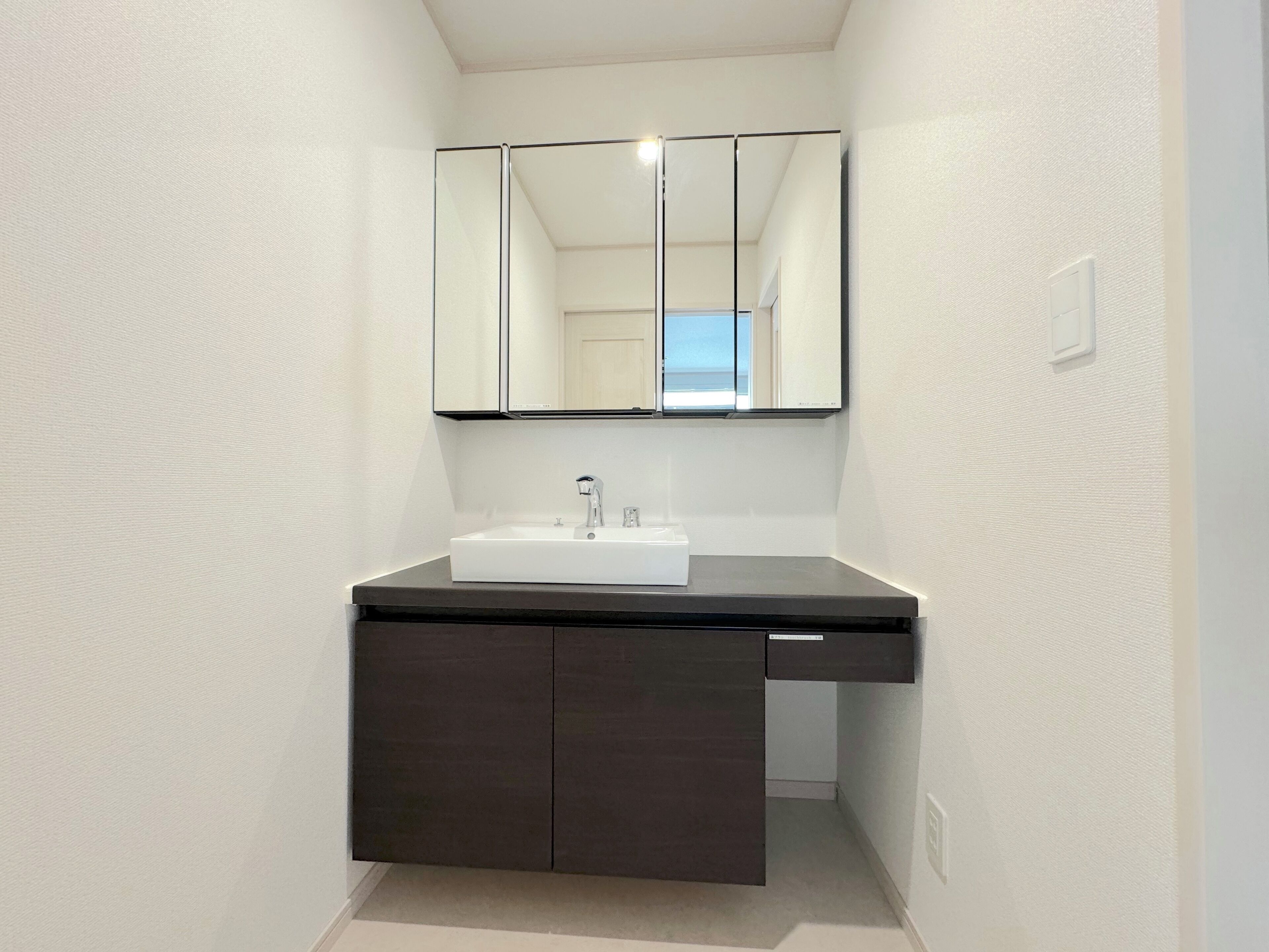 Une salle de bain moderne avec un lavabo blanc, des meubles de rangement aux couleurs sombres et un grand miroir au-dessus du lavabo.