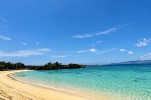 A beach with clear turquoise water, a sandy shore, and a forested island in the distance. - Grandioso Okinawa Pool Villa Onna 7 (Onna)
