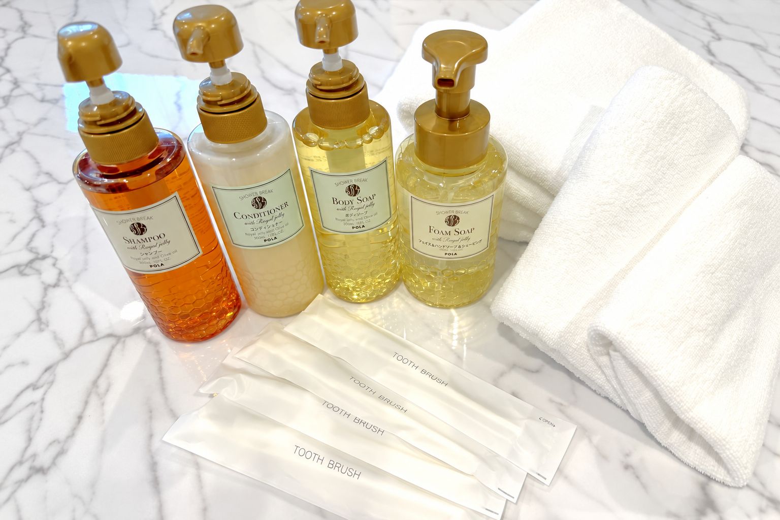 Four bottles of shower products and three toothbrushes on a marble surface.
