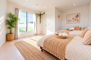 Une chambre avec un grand lit, une plante en pot, une vue à travers une porte coulissante et un tableau accroché au mur.