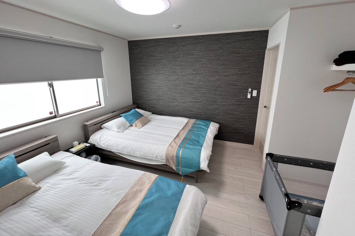 Moderni hotellihuone, jossa on kaksi sänkyä, suuri ikkuna, tumma tehosteseinä ja pieni vaatekaappi.