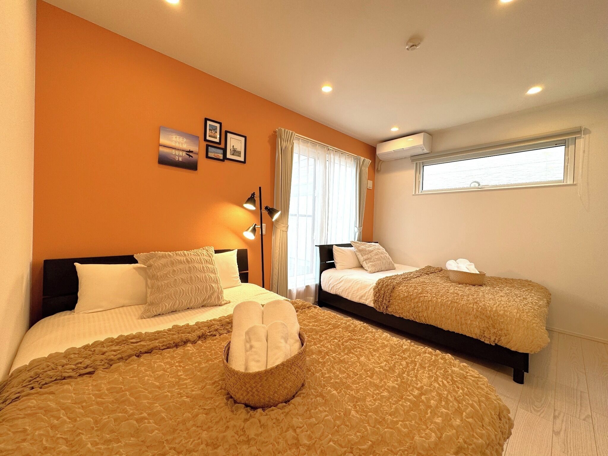 Een hotelkamer met twee bedden, een groot raam met gordijnen, een airconditioning en een wand met ingelijste foto's.